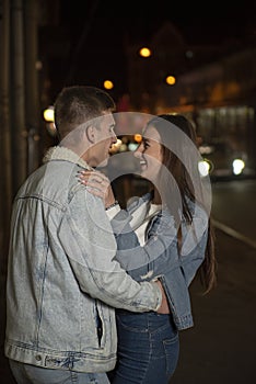 Laughing young people hug in the street. Evening date, young couple in love. Beautiful girl hugs a guy