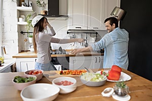 Laughing young spouses cooking food joking fighting on kitchen tools