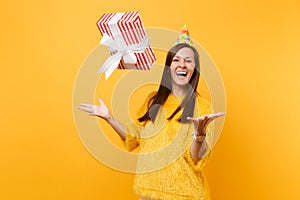 Laughing young woman in birthday party hat throwing up red box with gift present, celebrating and enjoying holiday