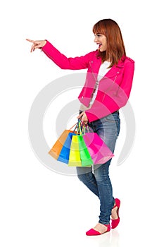 Laughing Young Woman Is Carrying Shopping Bags, Looking Away And Pointing