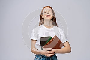 Laughing young woman college student with closed eyes holding books on isolated gray background.