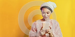 Laughing young woman girl in sweater and hat posing isolated on yellow background. Using mobile phone, typing sms message