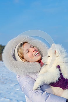 Laughing young woman and samoyed puppy kiss on winter frosty day