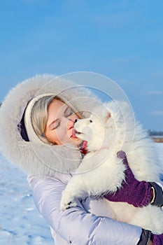 Laughing young woman and samoyed puppy kiss on winter frosty day