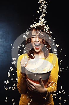 Laughing young woman staying under cheesy popcorn shower at cinema