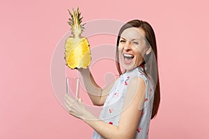 Laughing young woman in summer clothes holding half of fresh ripe pineapple fruit glass cup isolated on pink pastel wall