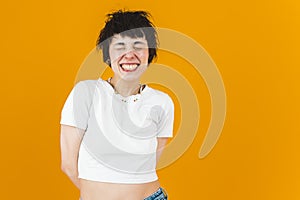Laughter concept. Amused short-haired girl in white t-shirt laughing with her eyes closed. Medium closeup studio shot