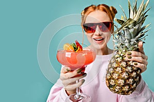 Laughting blonde woman in modern red sunglasses with strawberry margarita cocktail and a big pineapple at free text copy space