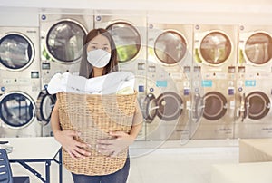 At a laundromat shop with many automatic washing machines, a beautiful woman wearing a mask is doing laundry