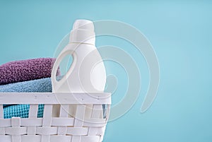 Laundry basket with a detergent bottle and a pile of clean towels on white table isolated on blue background