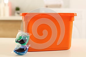 Laundry container and washing detergent capsules on table indoors