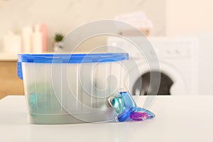 Laundry container and washing detergent capsules on table indoors