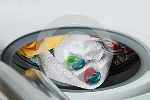 Laundry detergent capsules and clothes in washing machine drum, closeup view