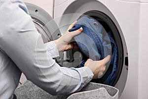 In laundry room female person loads dirty laundry items into washing machine