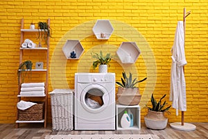 Laundry room interior with modern washing machine near yellow brick wall
