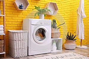 Laundry room interior with modern washing machine near yellow brick wall