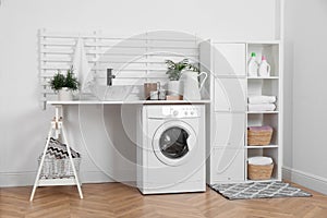 Laundry room interior with modern washing machine and shelving unit near white wall