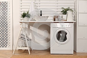 Laundry room interior with modern washing machine and shelving unit near white wall