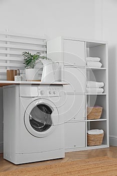 Laundry room interior with modern washing machine and shelving unit near white wall