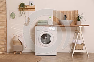 Laundry room interior with modern washing machine and stylish vessel sink on wooden countertop