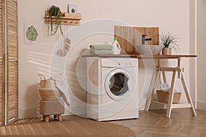 Laundry room interior with modern washing machine and stylish vessel sink on wooden countertop