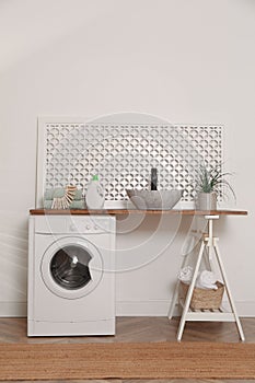 Laundry room interior with modern washing machine and stylish vessel sink on wooden countertop