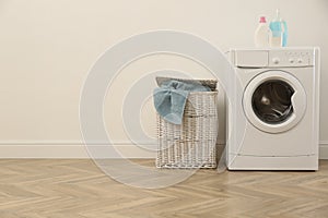 Laundry room interior with modern washing machine and wicker basket near white wall. Space for text