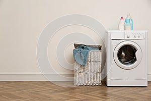 Laundry room interior with modern washing machine and wicker basket near white wall. Space for text