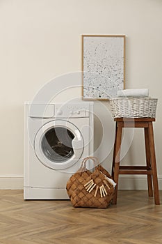 Laundry room interior with modern washing machine and wooden stool near white wall