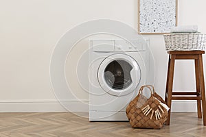 Laundry room interior with modern washing machine and wooden stool near white wall. Space for text