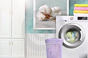 Laundry room interior with washing machine, basket, cotton towels, ambry and cotton flower photo in frame