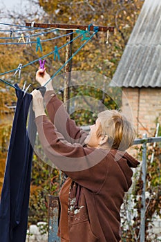 Laundry woman hangs clean wet cloth on clothes dryer after washing at home. Household chores and housekeeping