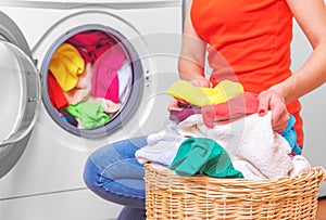 Young woman loads the laundry in the washing machine from the laundry basket before washing.