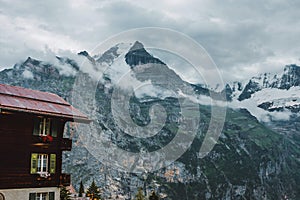 Lauterbrunnen, Switzerland, Jungfrau. Swiss Alps mountains. House with window shutters, flower boxes. Clouds, snow peaks