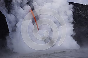 Lava flowing out of cliff into the ocean surounded by white cloud steam