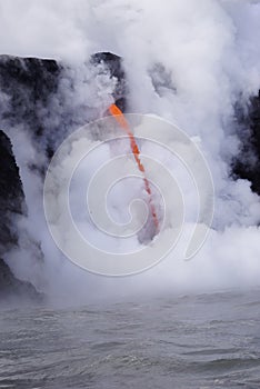 Lava flowing out of cliff into the ocean surounded by white cloud steam