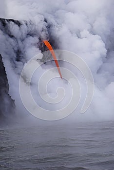 Lava flowing out of cliff into the ocean surounded by white cloud steam