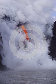 Lava flowing out of cliff into the ocean surounded by white cloud steam