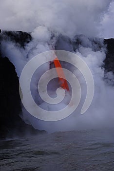 Lava flowing out of cliff into the ocean surounded by white cloud steam