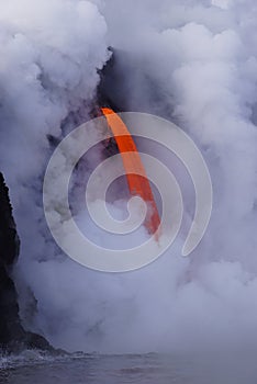 Lava flowing out of cliff into the ocean surounded by white cloud steam