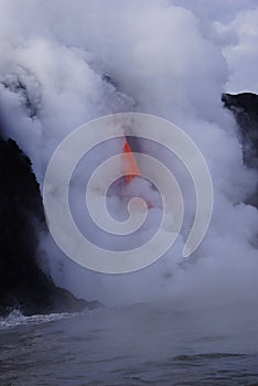 Lava flowing out of cliff into the ocean surounded by white cloud steam