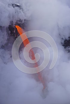 Lava flowing out of cliff into the ocean surounded by white cloud steam