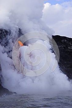 Lava flowing out of cliff into the ocean surounded by white cloud steam