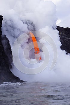 Lava flowing out of cliff into the ocean surounded by white cloud steam