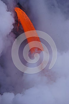 Lava flowing out of cliff into the ocean surounded by white cloud steam