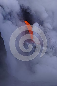 Lava flowing out of cliff into the ocean surounded by white cloud steam