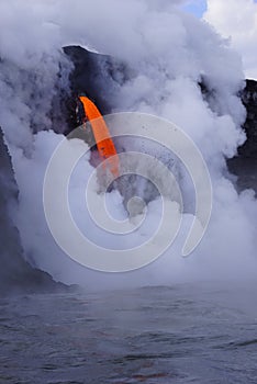 Lava flowing out of cliff into the ocean surounded by white cloud steam