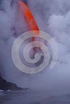 Lava flowing out of cliff into the ocean surounded by white cloud steam