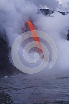 Lava flowing out of cliff into the ocean surounded by white cloud steam