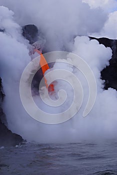 Lava flowing out of cliff into the ocean surounded by white cloud steam